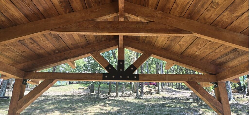 A wooden structure with a roof that is surrounded by trees.