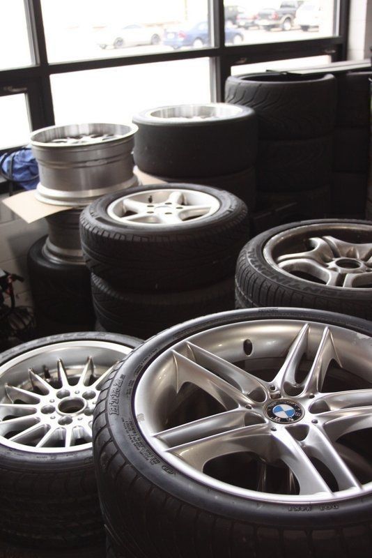 Tires and rims stacked in a garage, including several BMW rims.