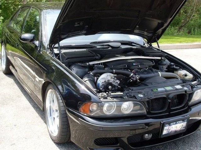 Black BMW sedan with hood open, revealing engine components. Parked outdoors on pavement.