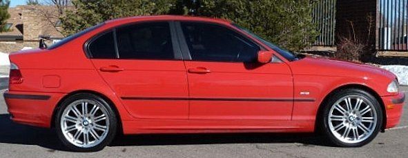 Red BMW sedan with silver rims parked outside on a sunny day.