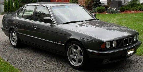 Gray BMW sedan parked on a paved driveway next to a grassy area.