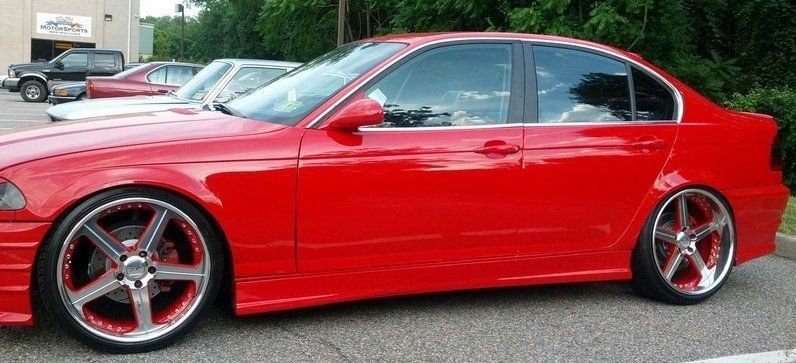 Red car with custom wheels parked on asphalt.
