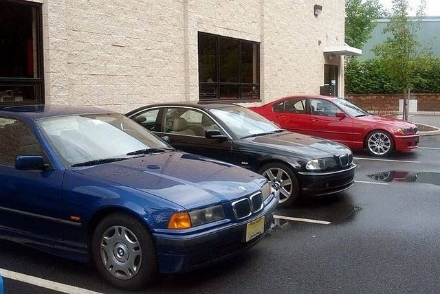 Three parked BMW sedans in blue, black, and red, in front of a building.