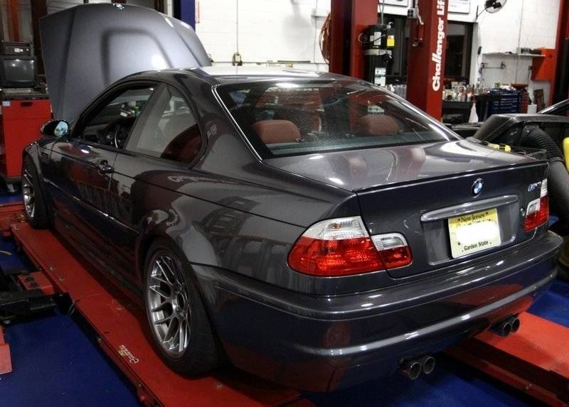 Dark gray BMW coupe on a lift with the hood open in a garage.