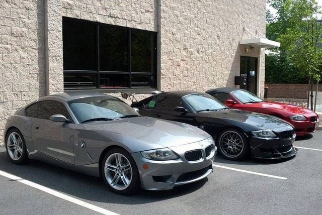 Three parked BMW Z4 coupes: silver, black, and red, in front of a building.