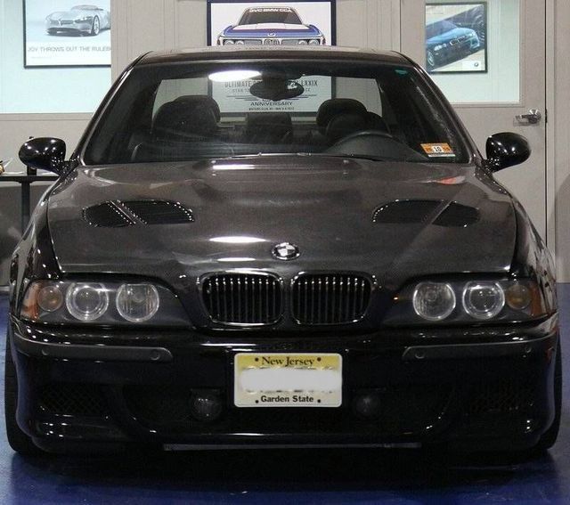 Black BMW M5 with a carbon fiber hood, New Jersey license plate, parked indoors.