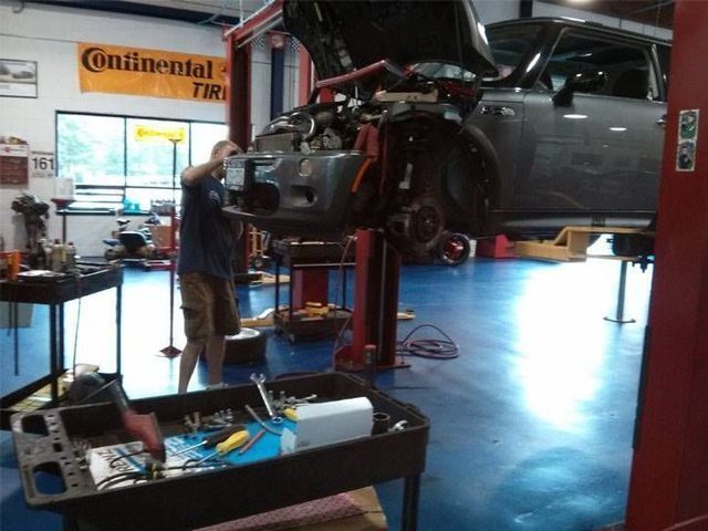 Mechanic working on a gray car raised on a lift in a garage. Tools in tray on the floor.