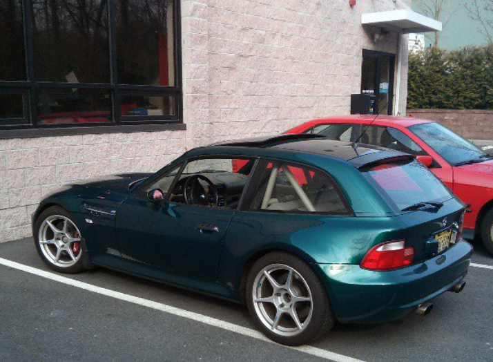 Dark green BMW Z3 coupe parked next to a red car in a parking lot, near a building.