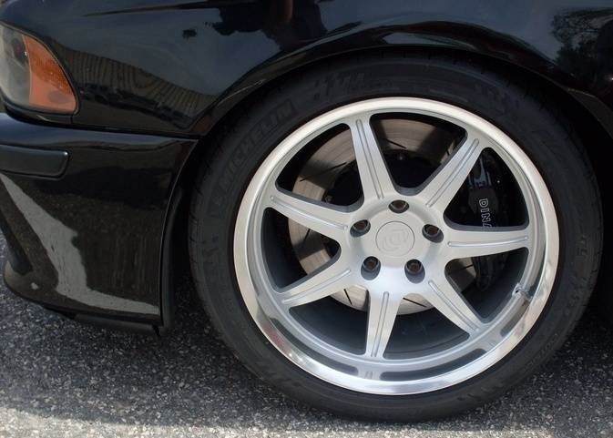 Black car's front wheel with silver alloy rim and black tire parked on asphalt.