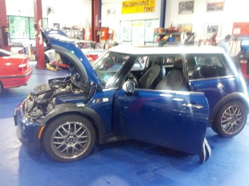 Blue Mini Cooper with open hood and door in a repair shop.