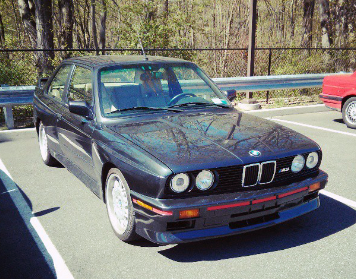 Dark blue vintage BMW M3 parked on asphalt, sunny day.