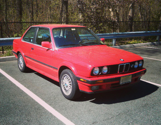 Red BMW E30 coupe parked in a parking lot, sunny day.