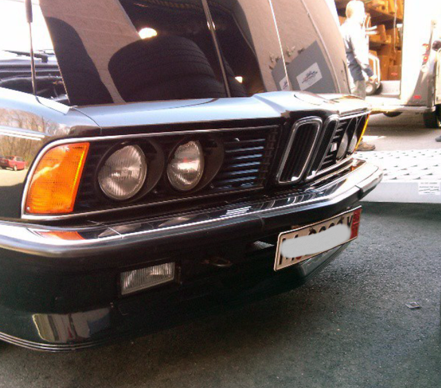 Front of a vintage black BMW car with orange turn signal, two headlights, and an open hood.