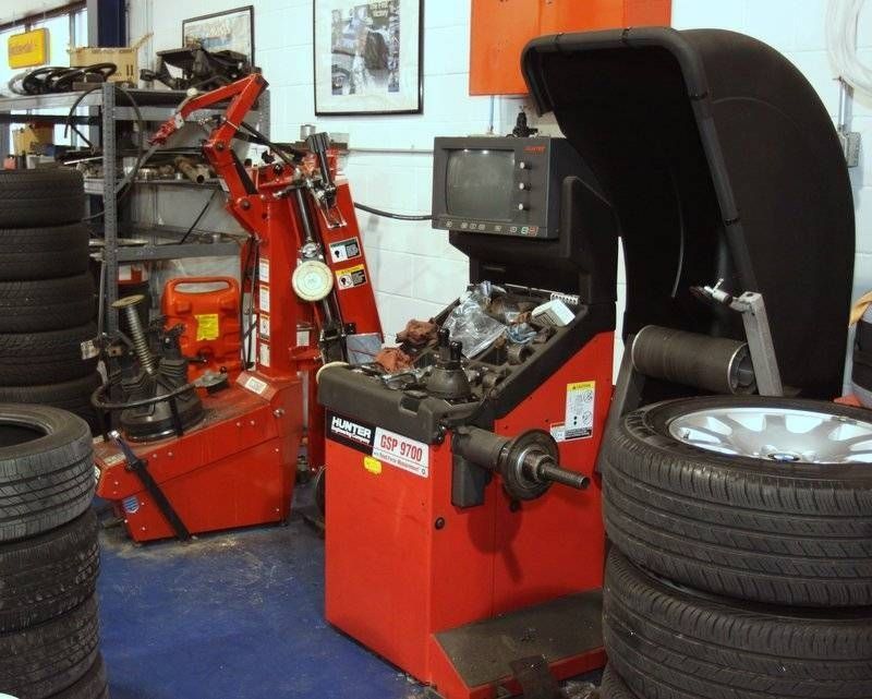 Tire shop interior. Red tire balancing machine with a wheel; stacks of tires, and other equipment.
