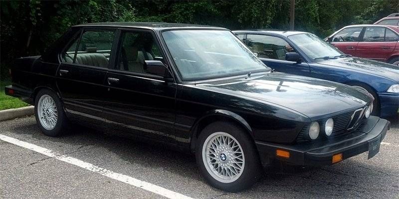 Black BMW sedan parked in a parking lot, with other cars nearby.