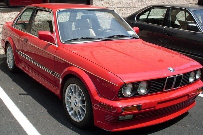 Red BMW coupe parked in a lot, with silver rims and black trim.