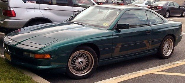 Green BMW 8-Series coupe parked in a lot.  Silver rims, tinted windows, and light-colored parking lines.