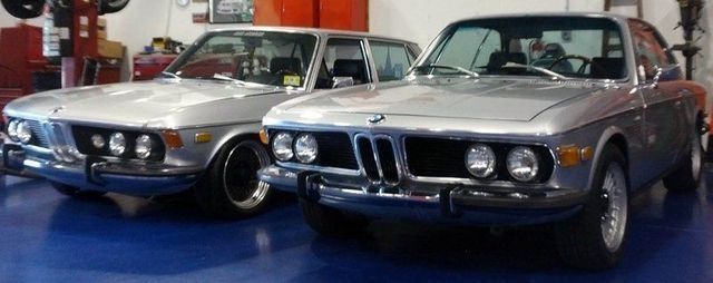 Two silver BMW coupes in a garage, side-by-side.