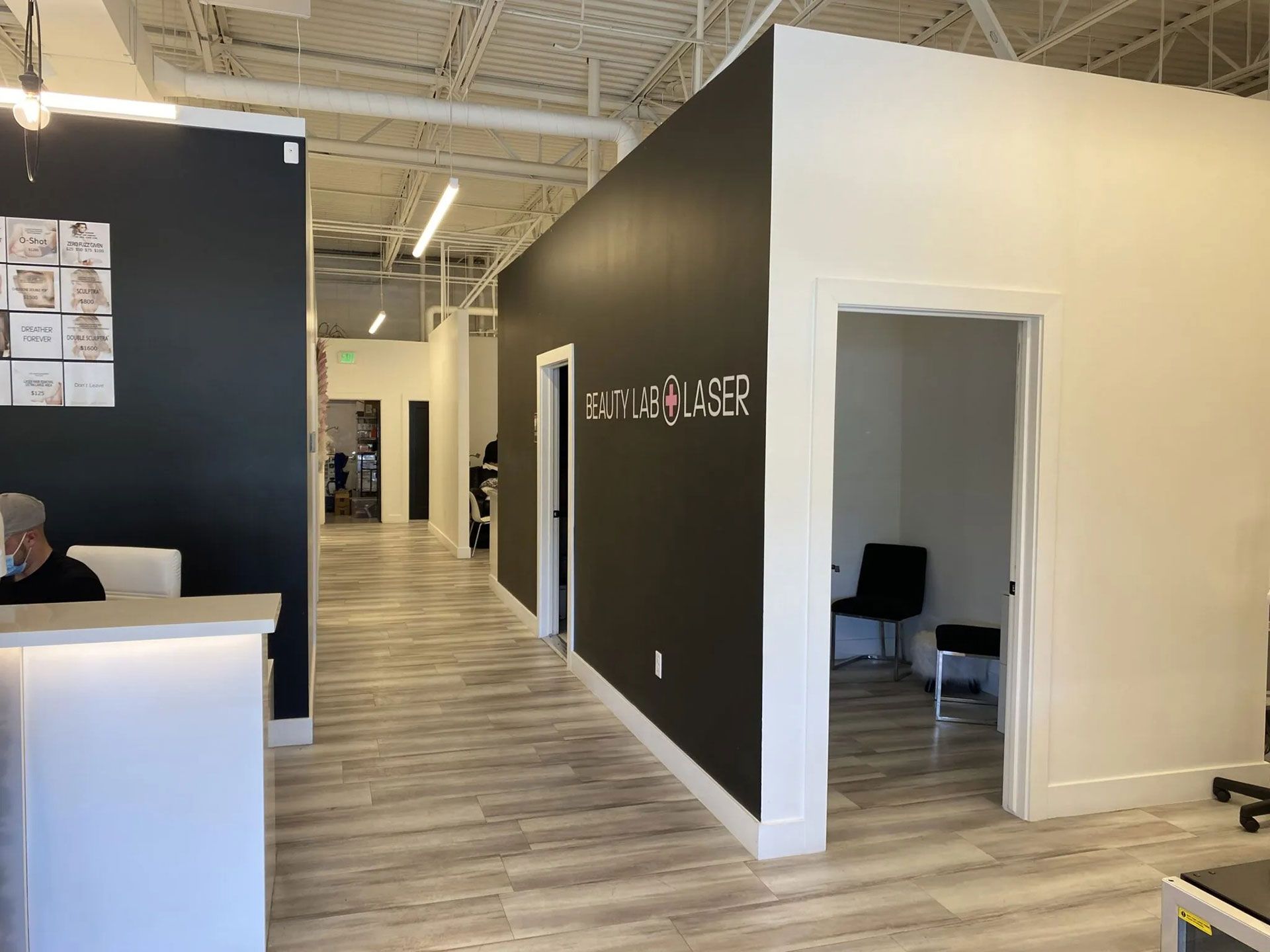 Modern office interior with a white reception desk, black accent walls, light wood floors, and open doorways to rooms.