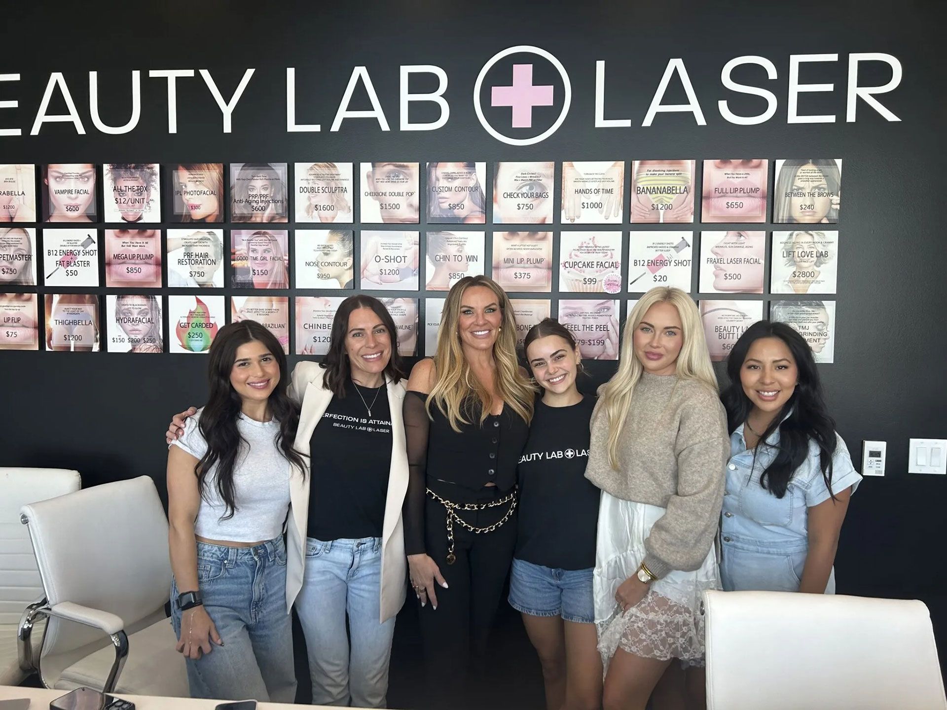 Six people stand in front of a Beauty Lab + Laser wall sign featuring a grid of portrait photos.
