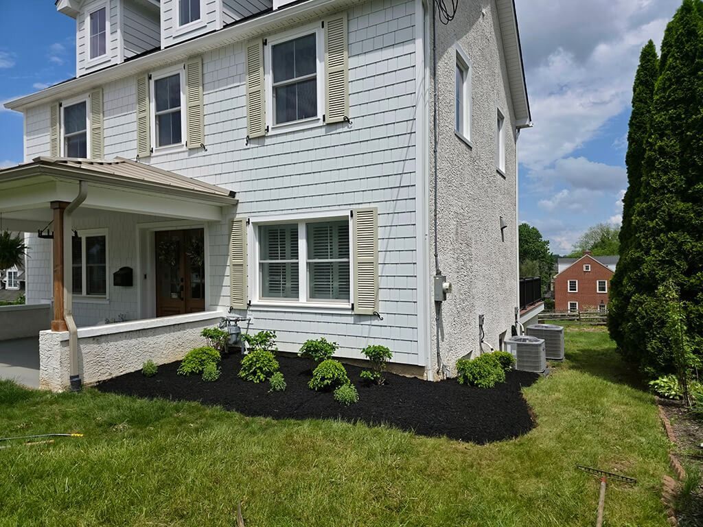 White two-story house with a covered porch, green lawn, and black mulch landscaping under a partly cloudy sky