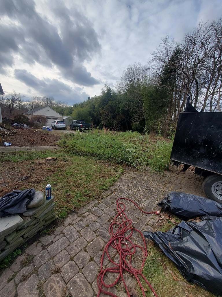 Rural path with coiled red rope in the foreground, tarps and debris at sides, cloudy sky overhead