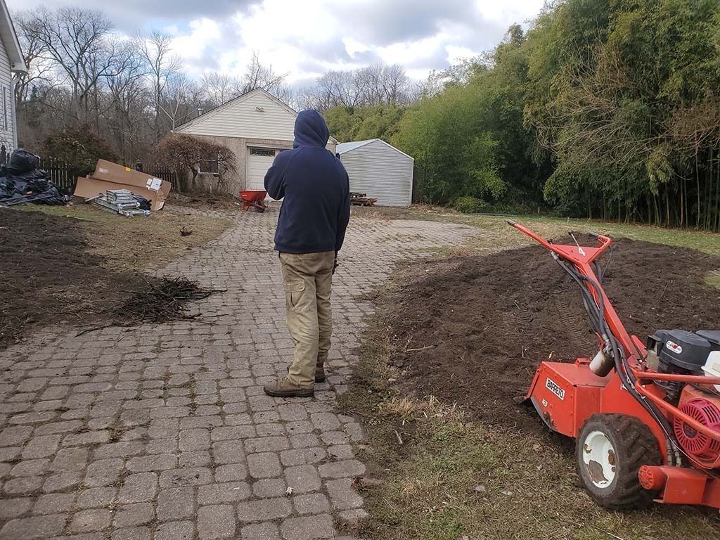 Person walking on muddy driveway with a red tiller in the foreground and a white tent-like structure ahead