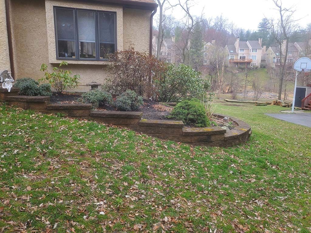 Suburban yard with a house, raised flower bed, and a lawn covered in fallen leaves