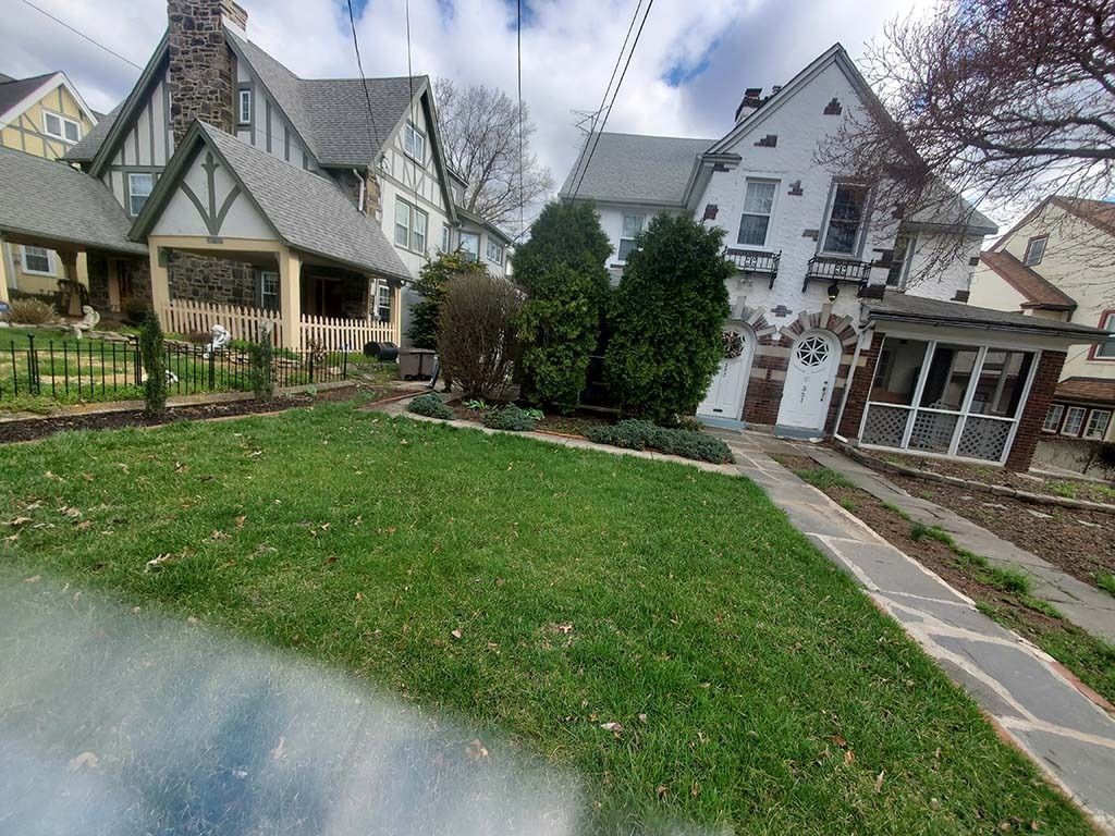 Residential front yard with green lawn, stone walkway, and Tudor-style houses under a cloudy sky
