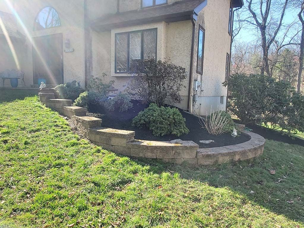 Sunlit house entry with stone steps, curved retaining wall, and green lawn under bare trees