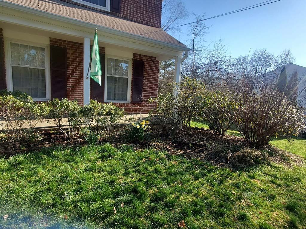 Brick house with green lawn, shrubs, and a front porch in bright sunlight
