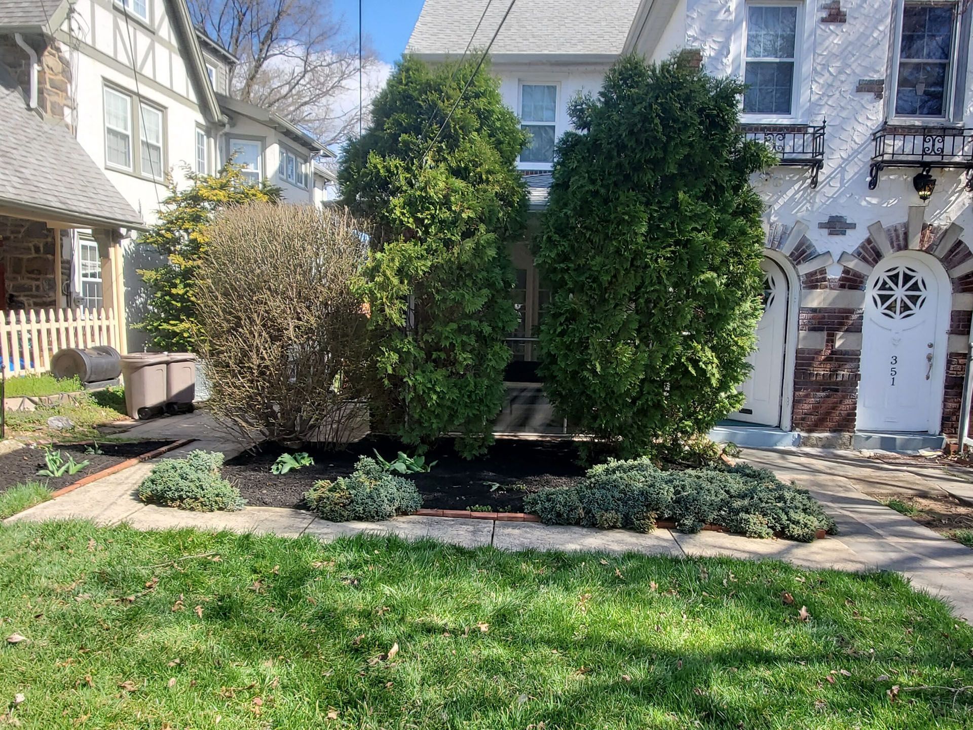 Front yard with manicured shrubs, green lawn, and stone walkway beside a white house