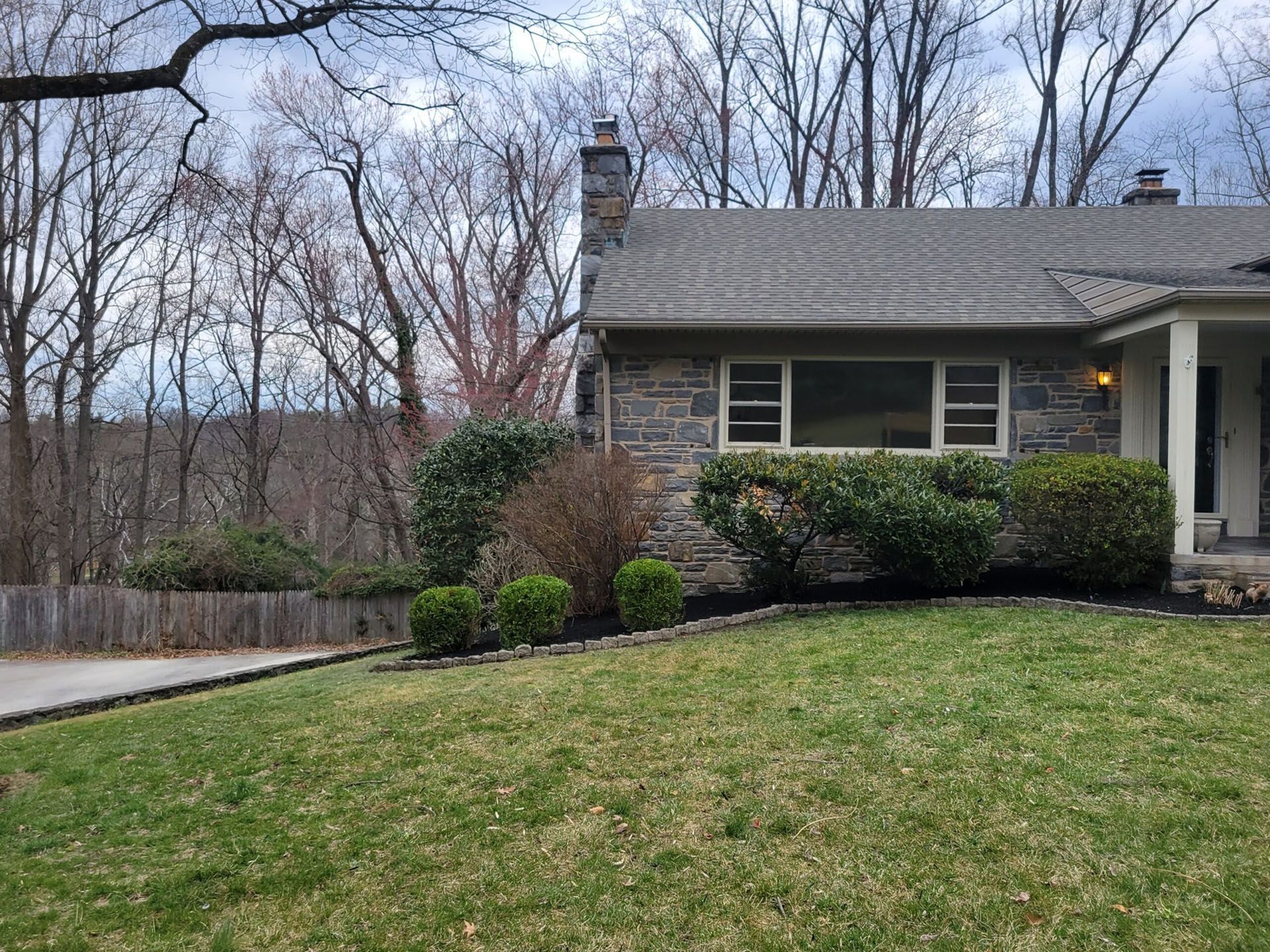 Suburban house with gray roof, green lawn, and bare trees on an overcast day