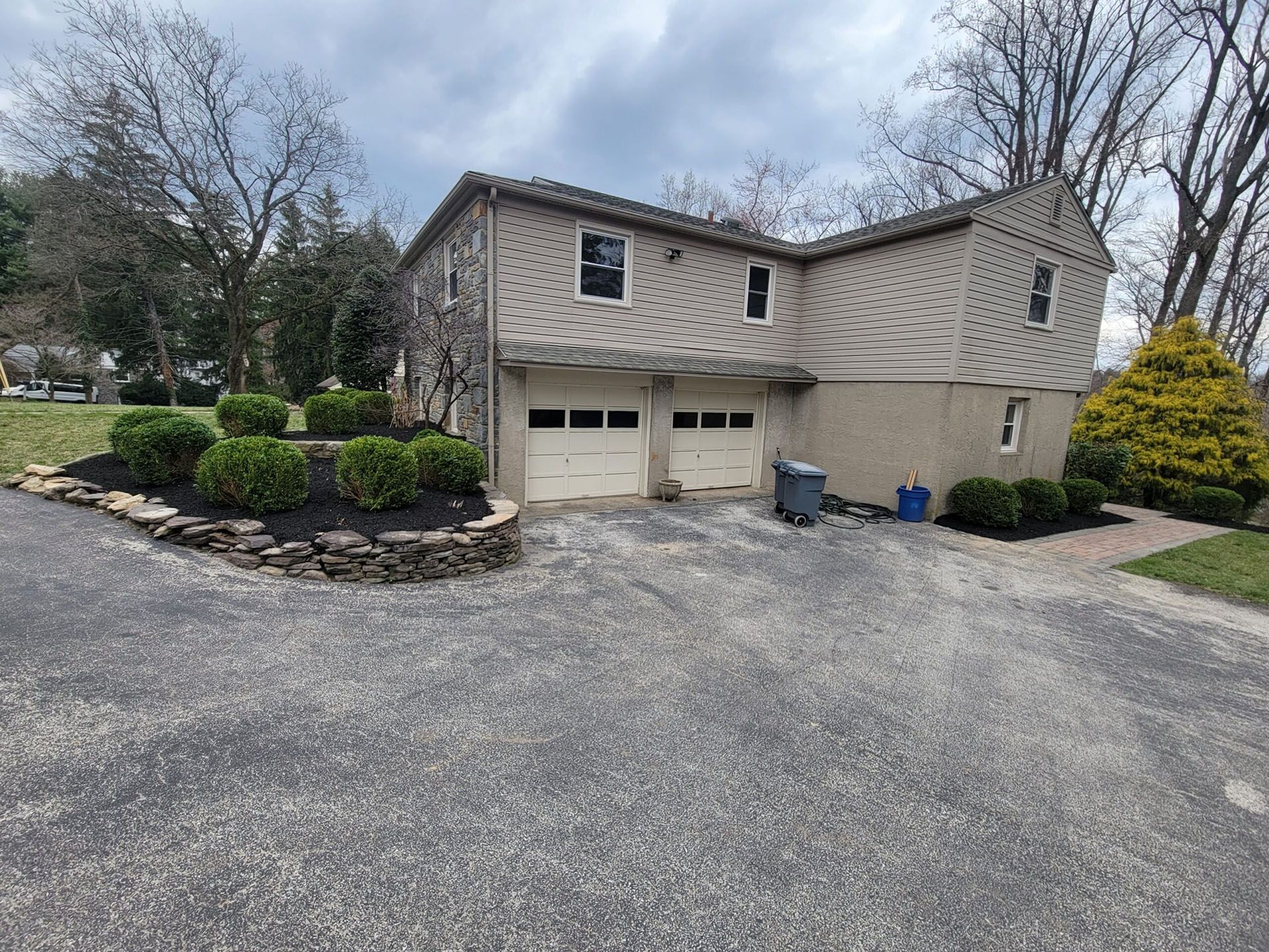 Suburban two-story beige house with attached garage, gravel driveway, and landscaped front yard