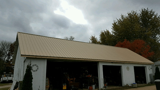 A white barn with a metal roof and a cloudy sky in the background.
