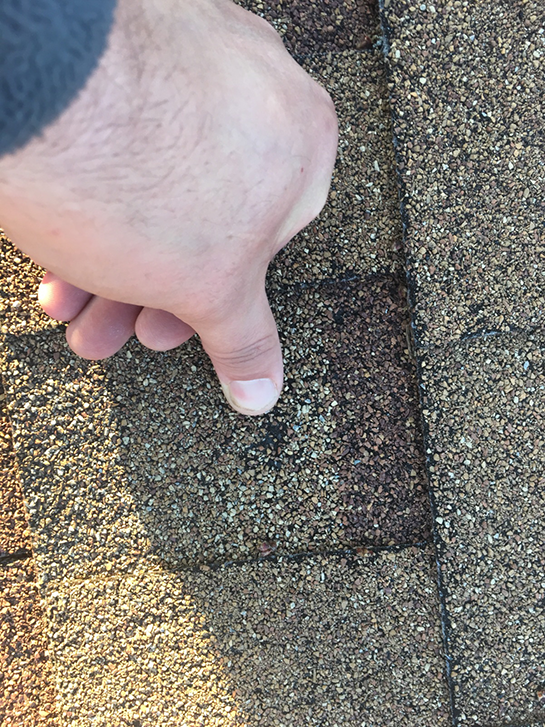 A person is pointing at a hole in a roof shingle.