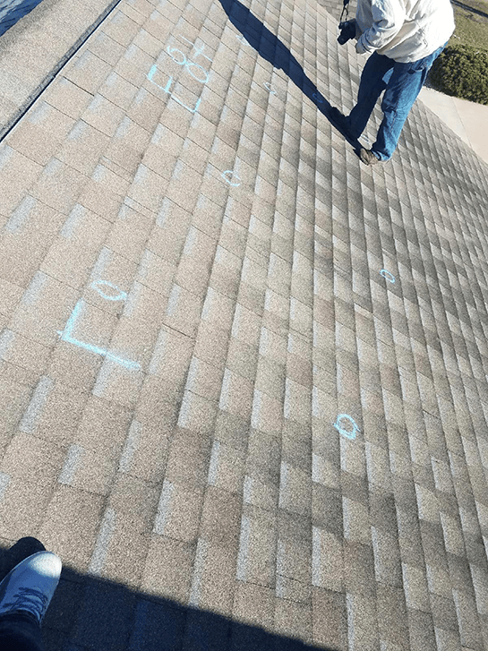 A man is standing on the roof of a house looking at the shingles.