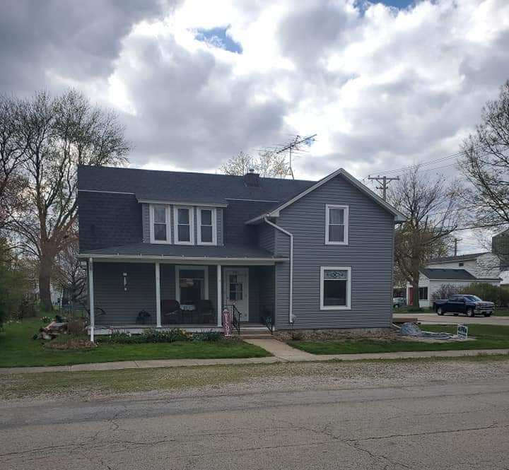 A gray house with a black roof and a porch on a cloudy day.