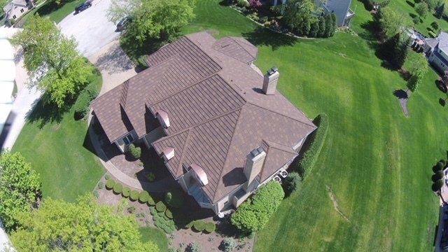 An aerial view of a large house with a brown roof in a residential area.