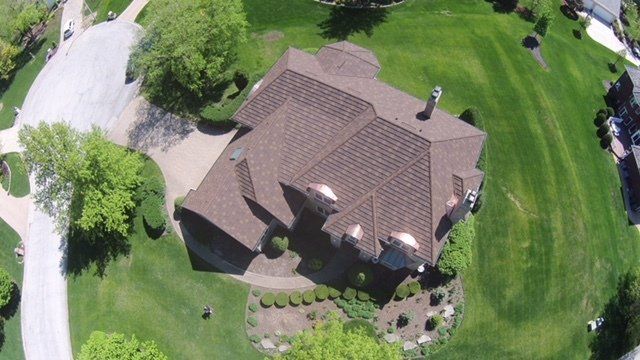 An aerial view of a large house with a brown roof in a residential area.