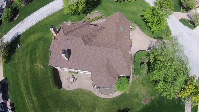 An aerial view of a house with a brown roof in a residential area.