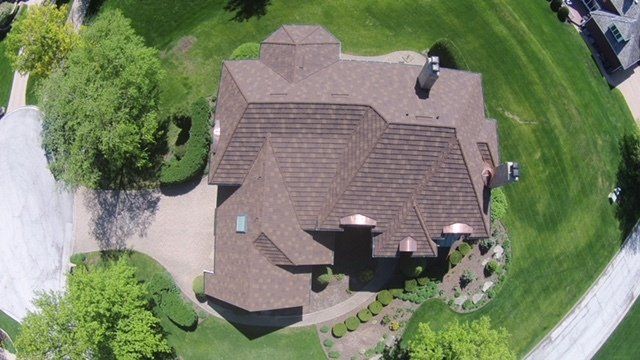 An aerial view of a large house with a brown roof surrounded by trees and grass.