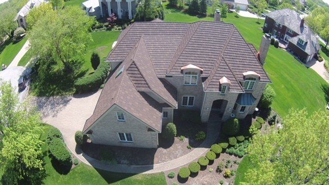 An aerial view of a large house with a brown roof in a residential area.