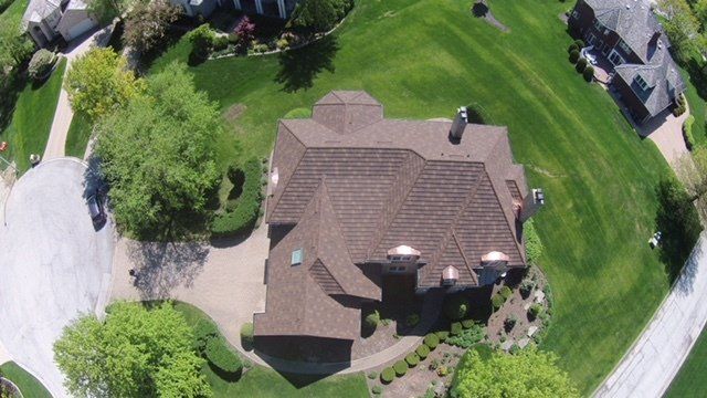 An aerial view of a large house in a residential area surrounded by trees.