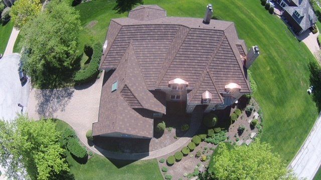 An aerial view of a house with a brown roof in a residential area.