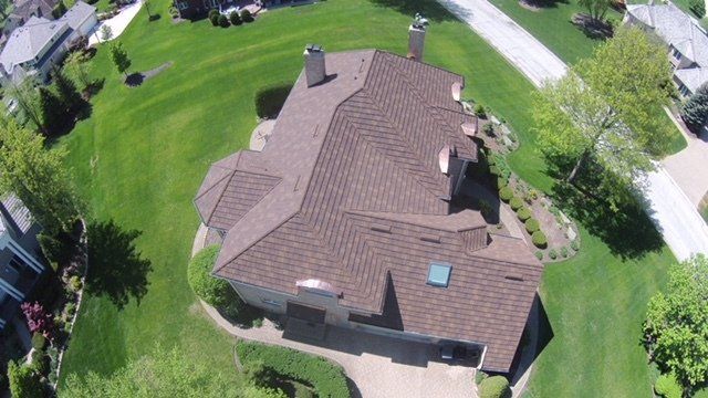 An aerial view of a house with a brown roof in a residential area.