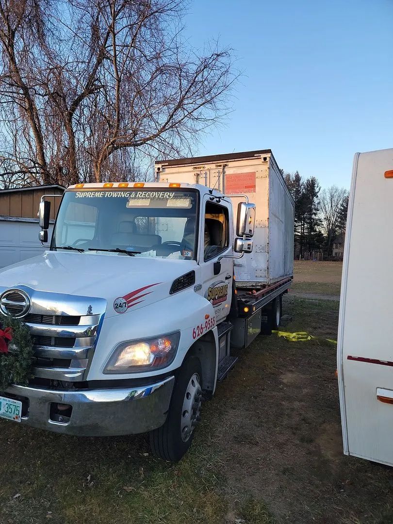 A white tow truck is parked in a grassy field next to a trailer.