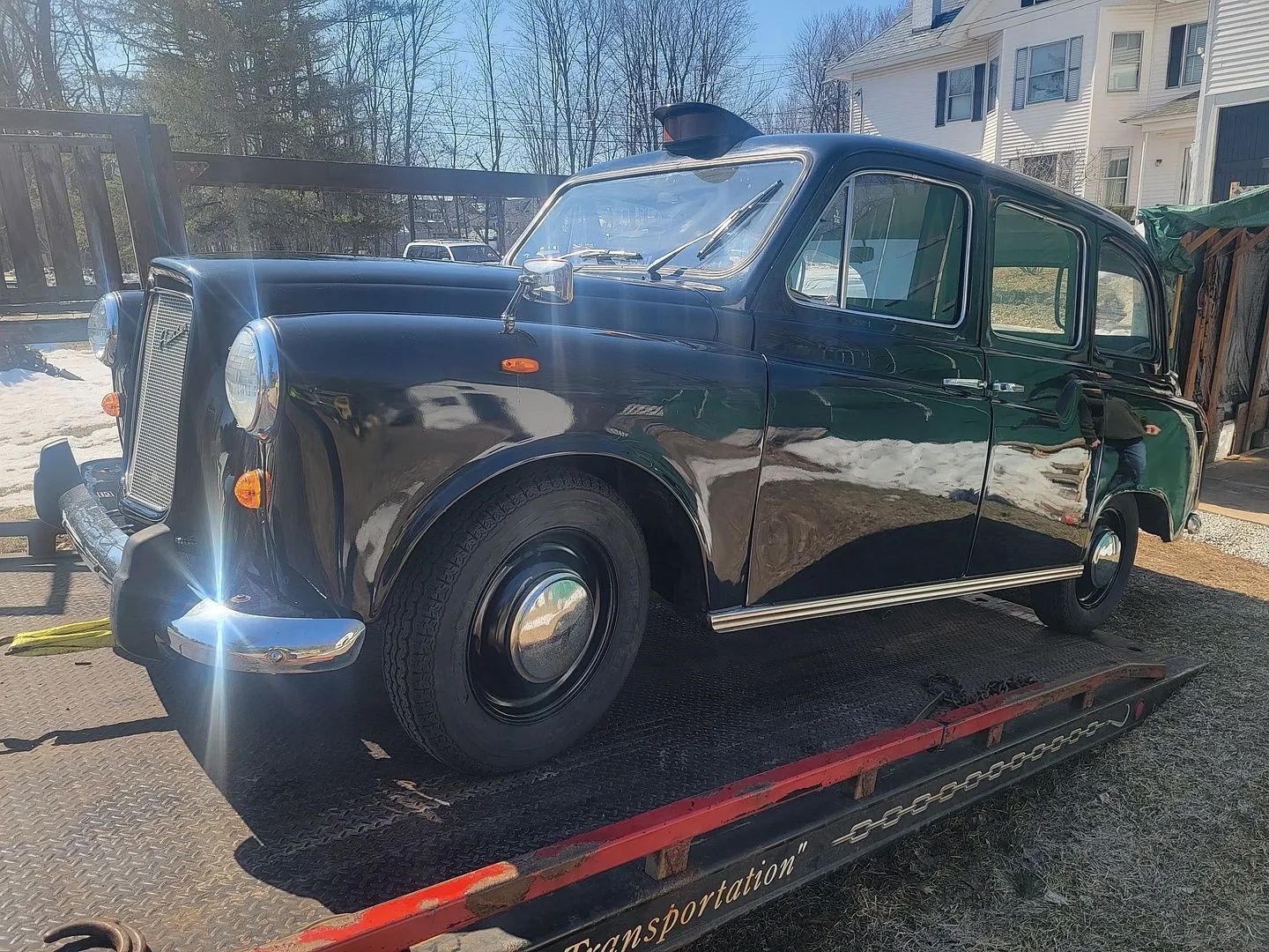 A black taxi cab is sitting on top of a tow truck.