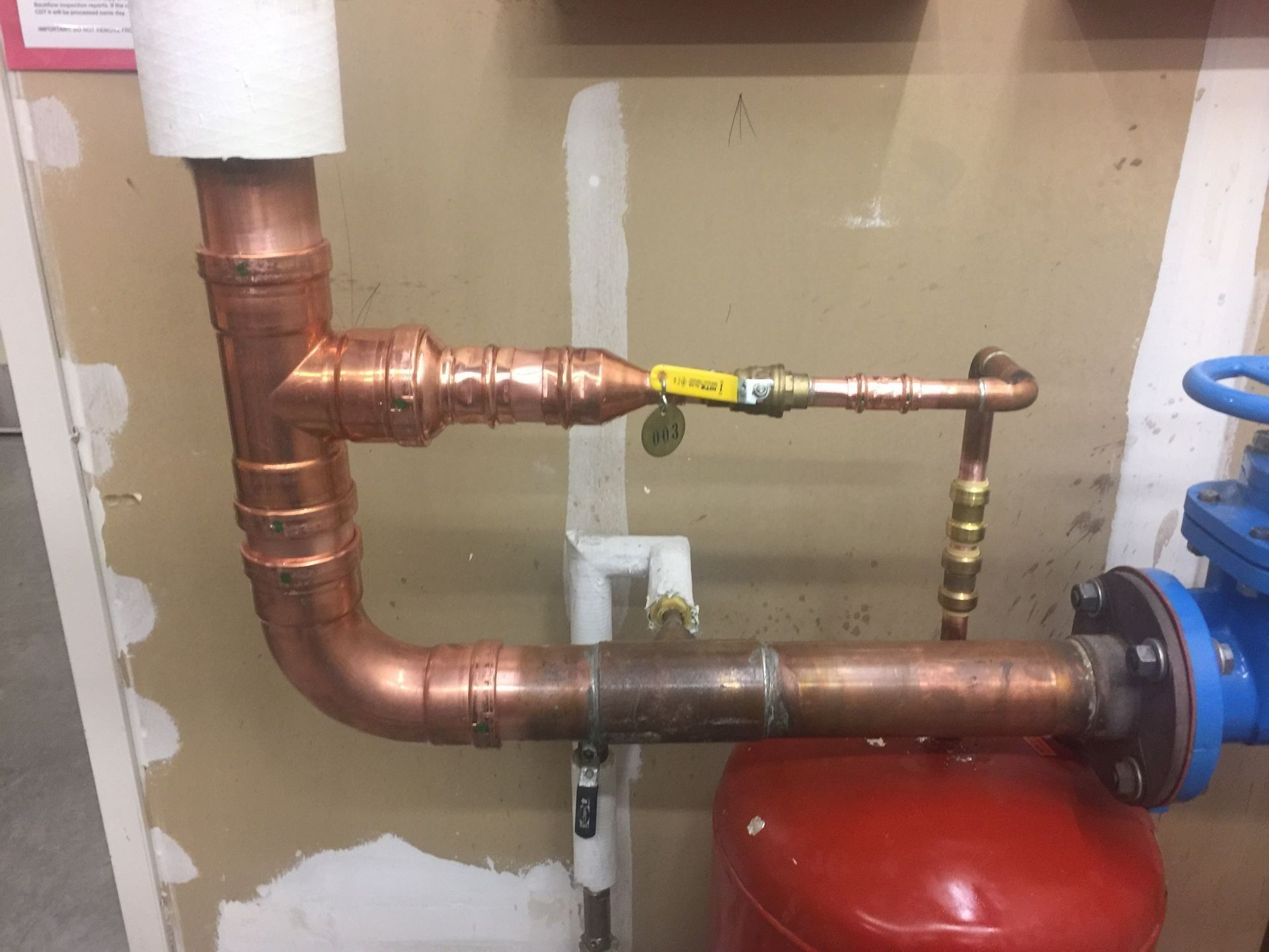 Copper pipes with a yellow valve and red tank, indoors.