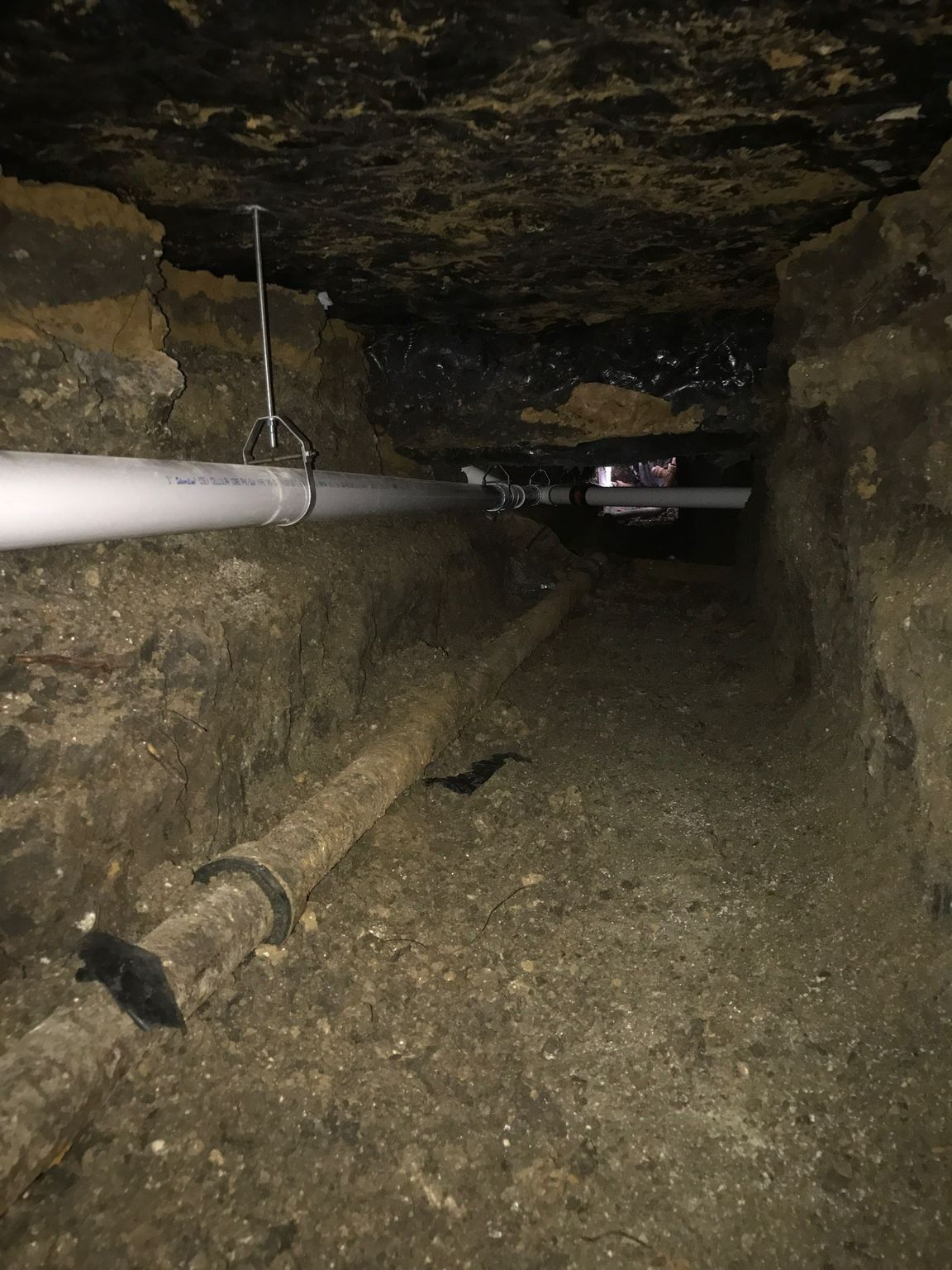Underground view: White PVC pipe and old rusty pipe in a dirt tunnel.